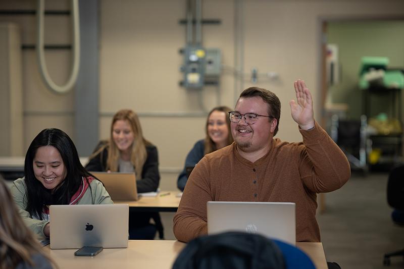 一个穿着棕色衬衫的微笑的学生在课堂上举手