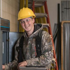 一位电气技术专业的学生戴着黄色安全帽，面带微笑